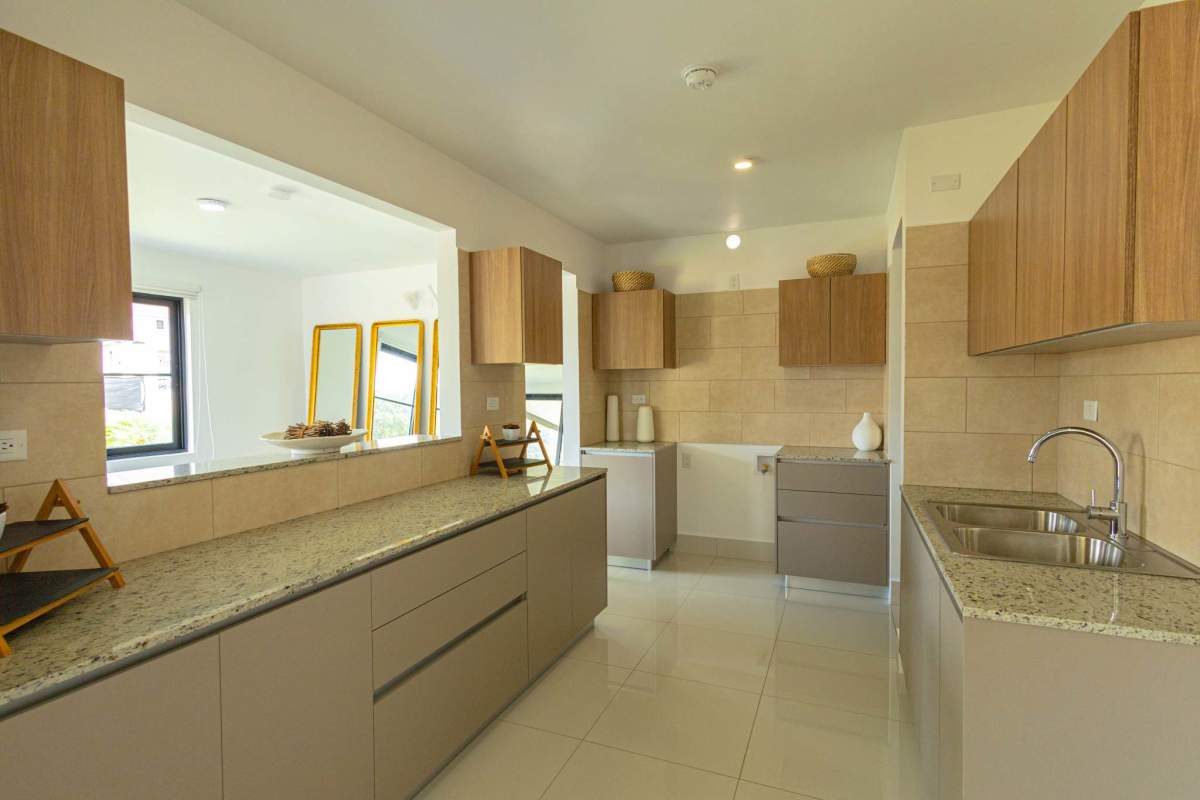 Modern kitchen with granite countertops, wood cabinetry, and pass-through window in Arcadia Costa Verde home