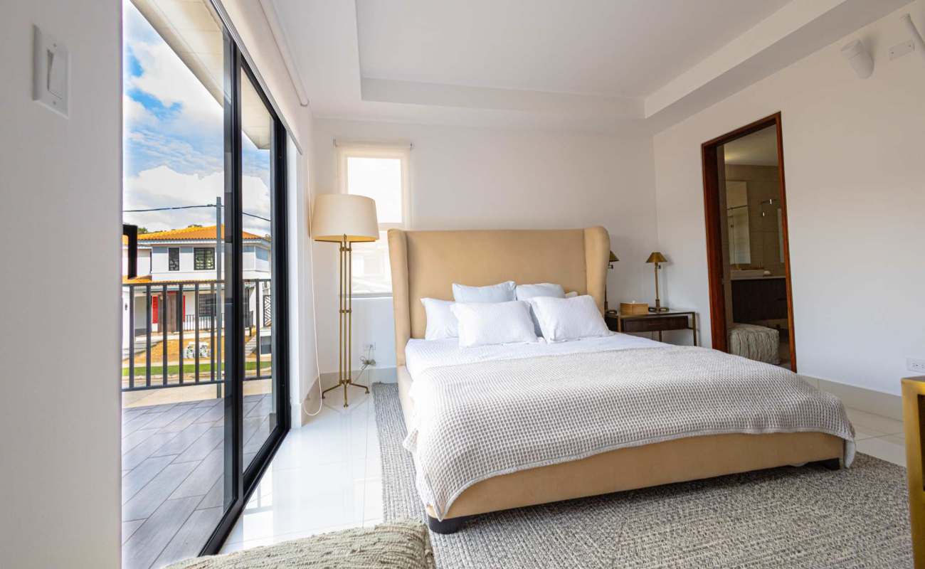 Large bedroom with sliding glass doors opening to balcony and neutral minimalist decor in Arcadia Costa Verde