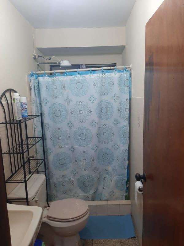 Small bathroom with shower, toilet, sink, and metal shelf in PH Los Nazareth Tumba Muerto Panama