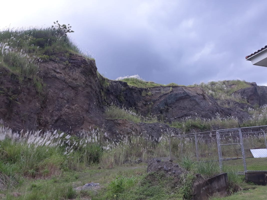 Rocky terrain and overgrown grass next to fence with skyline views near Bahai Temple Panama.