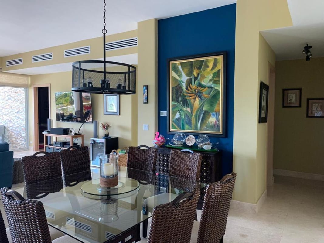 Open-plan coastal dining with glass table, woven chairs, blue accent wall, living room at Bijao Beach Condo