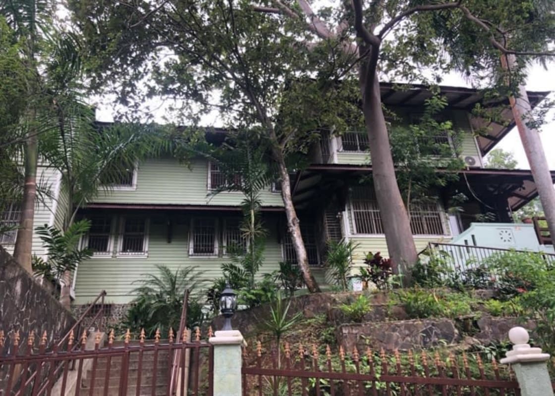 Two-story green colonial style house surrounded by lush garden and iron fence in Ancon Panama