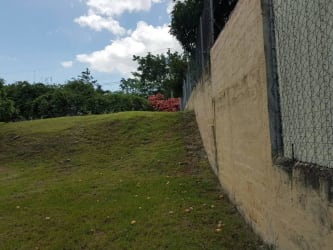 Grassy sloped residential lot with perimeter fence and retaining wall in Costa Esmeralda San Carlos Panama