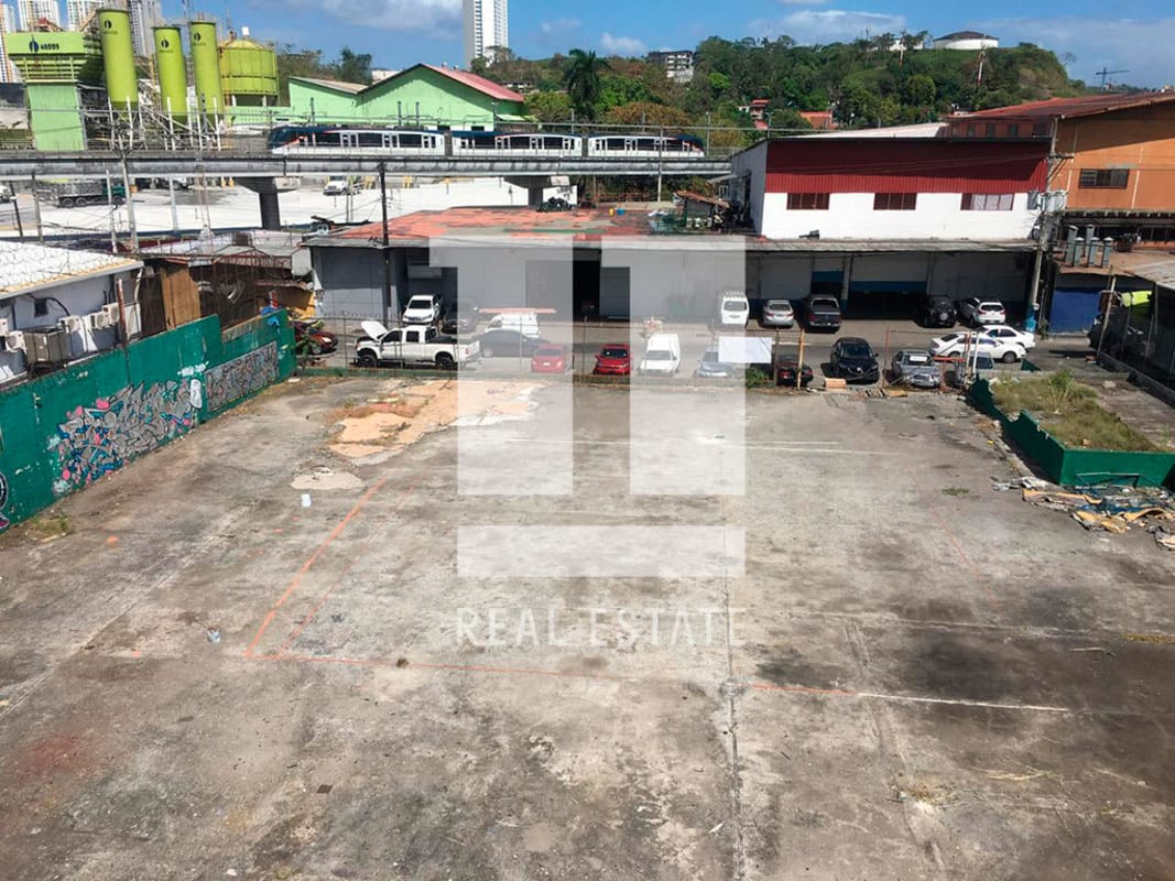 Vacant paved lot adjacent to industrial and commercial areas with fencing and urban surroundings