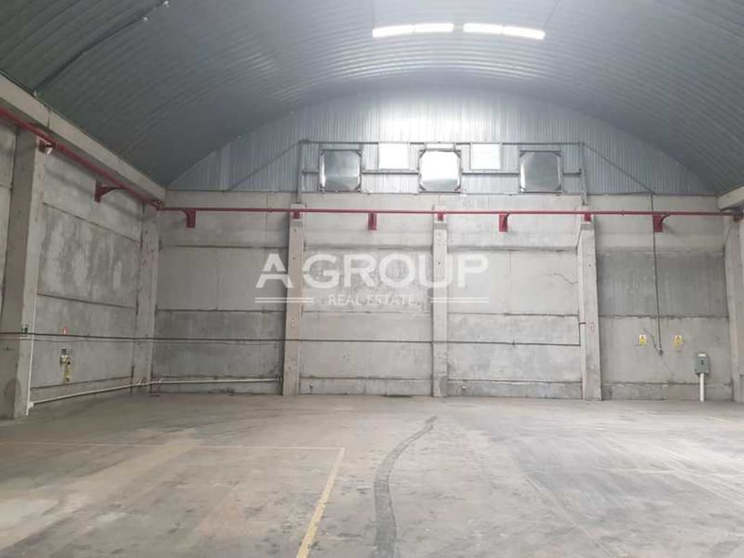 Empty warehouse with curved metal roofing, concrete walls, ventilation and lighting