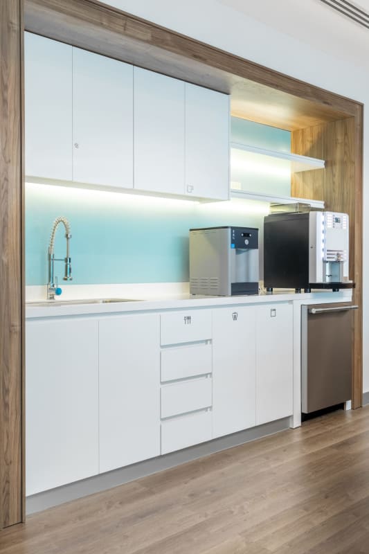 Small kitchenette with white cabinets wooden accents blue backsplash in office tower Panama