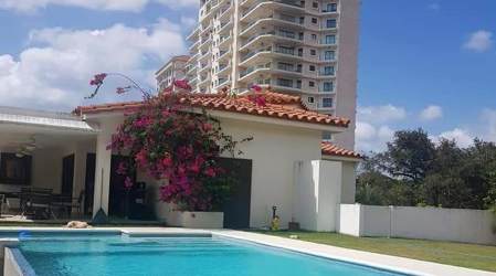 Mediterranean villa with terracotta roof, garden, pool and luxury tower behind in VistaMar Panama