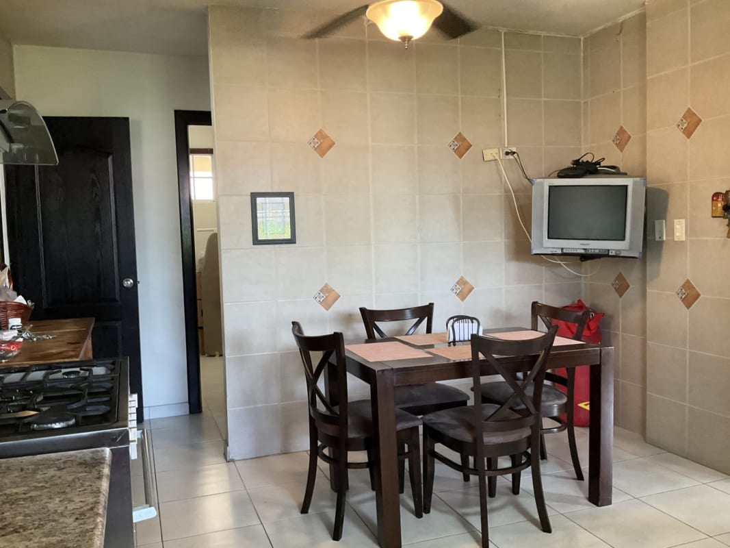 Kitchen dining with wooden table, ceramic tile wall, TV mount, window blinds Castel Novo home Panama