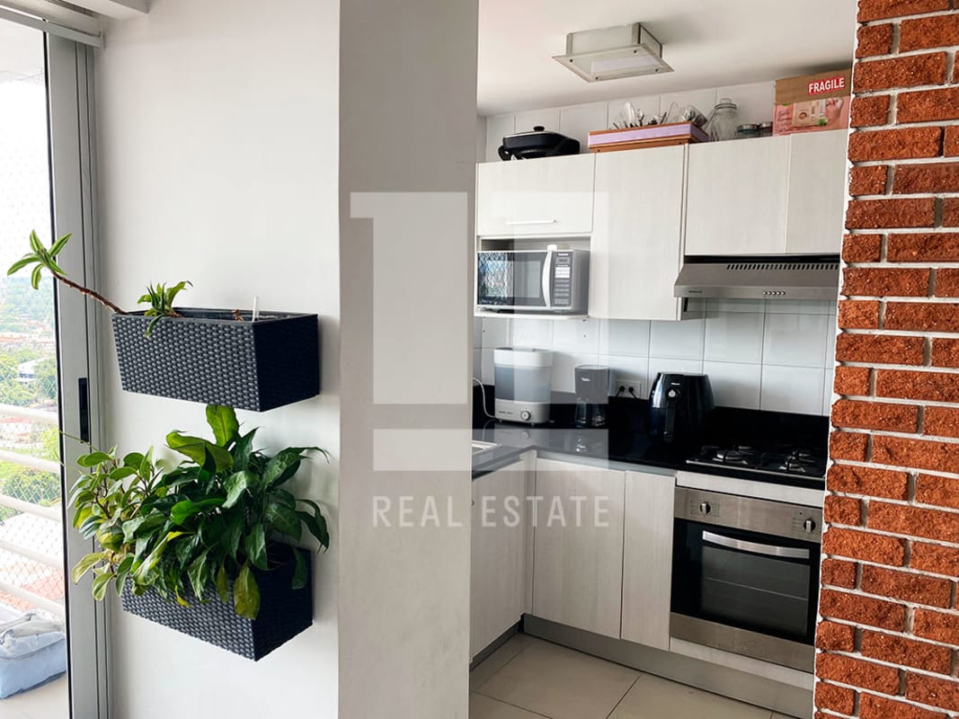 Kitchen with white cabinetry, black countertops, and brick accent wall PH Sky Level Hato Pintado Panama
