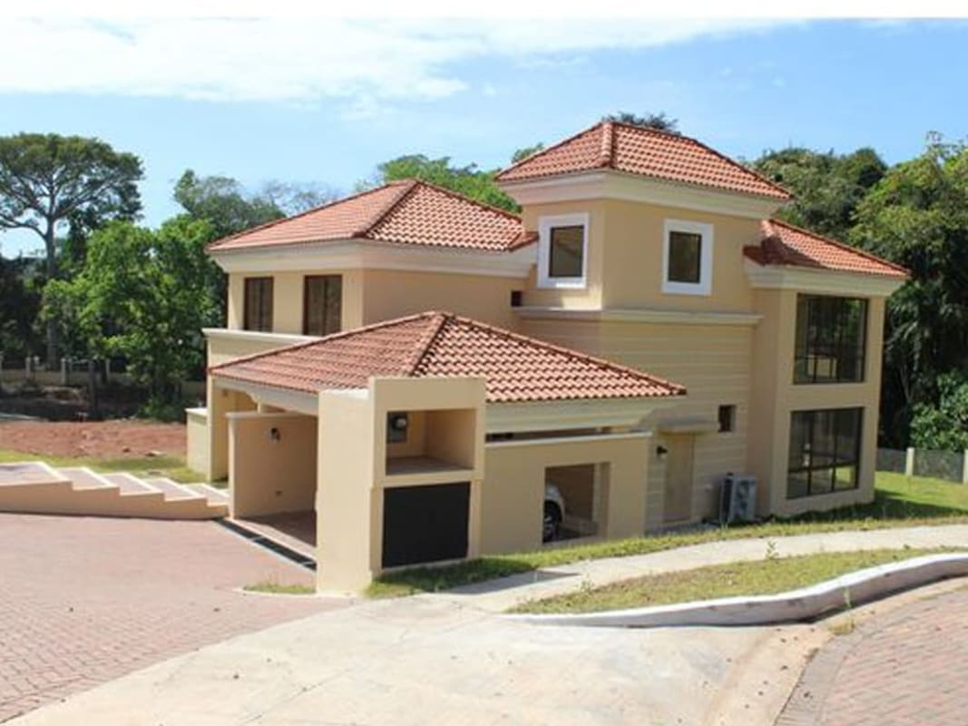 Multi-story Mediterranean house with large windows, tiled roof, garage, lush forest backdrop