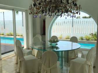 Elegant dining with chandelier, glass table, slipcovered chairs overlooking pool Santa Clara Panama