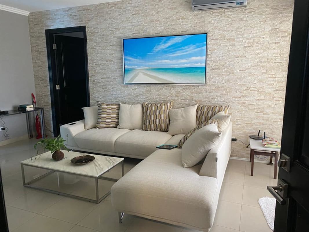 Modern living room with beige sectional sofa, stone wall, oceanfront balcony at PH Zeus Costa del Este