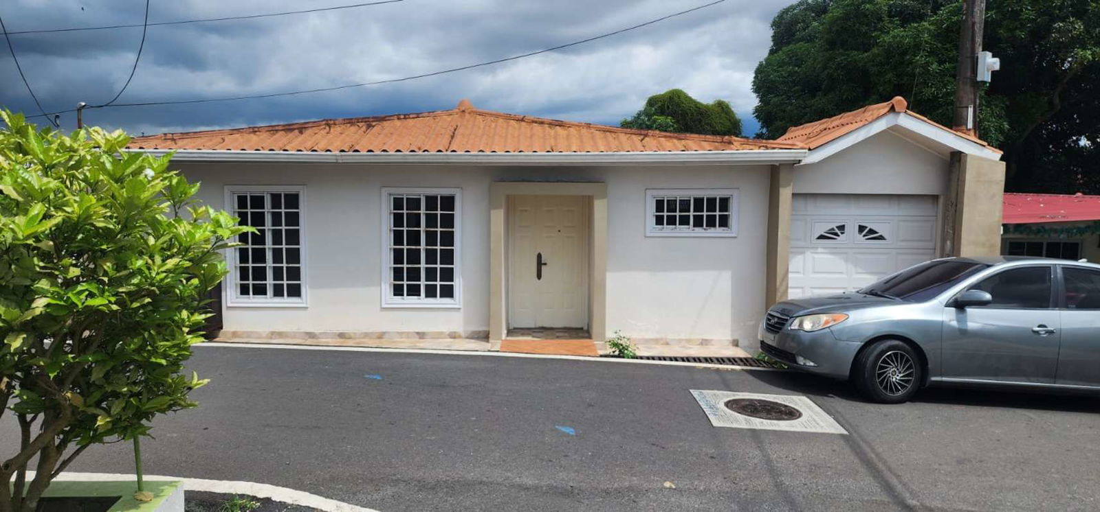 Single-story white house with terracotta roof, driveway and greenery in Pedregal Panama