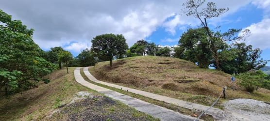 Grassy slope with paved trail surrounded by trees, mountain sky in Altos del María Panama