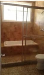 Bathroom with tiled walls, bathtub with sliding door, window, and toilet in Howard house rental Panama