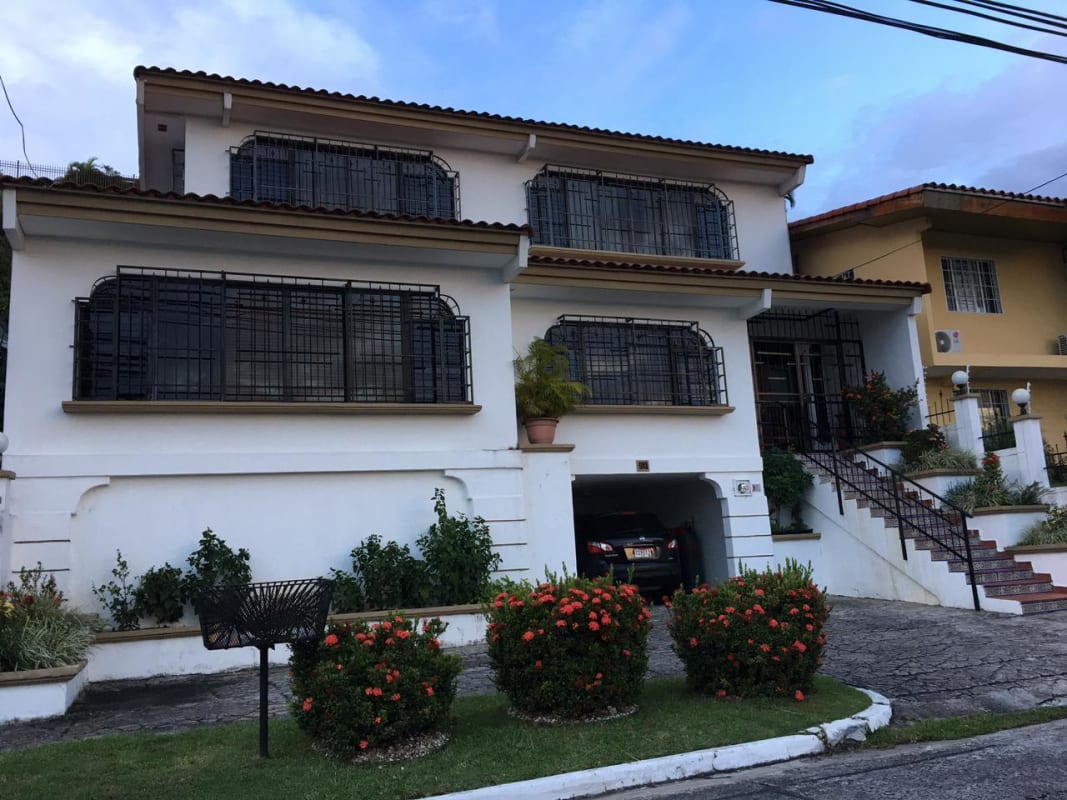 Front view two-story home with tiled roof, front garden, driveway in Panama City neighborhood