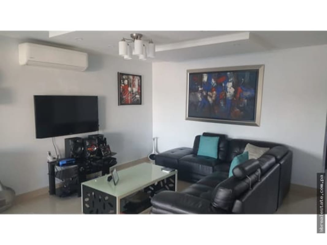 Living room with black sectional sofa, TV and art in Green Villas Las Cumbres Panama