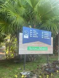 Informational sign surrounded by palm trees and tropical garden community entrance at Altos del María