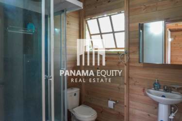 Rustic bathroom with wooden paneling, glass shower enclosure, pedestal sink in El Valle mountain cabin Panama