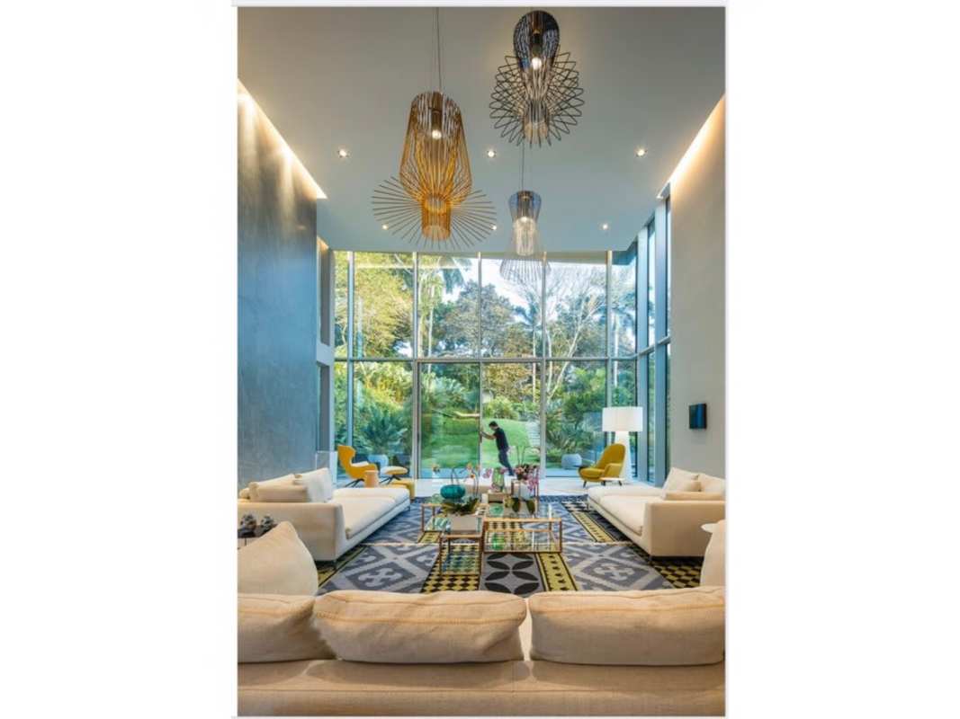 Double-height living room with floor-to-ceiling windows, cream sofas, yellow chairs in luxury Panama home
