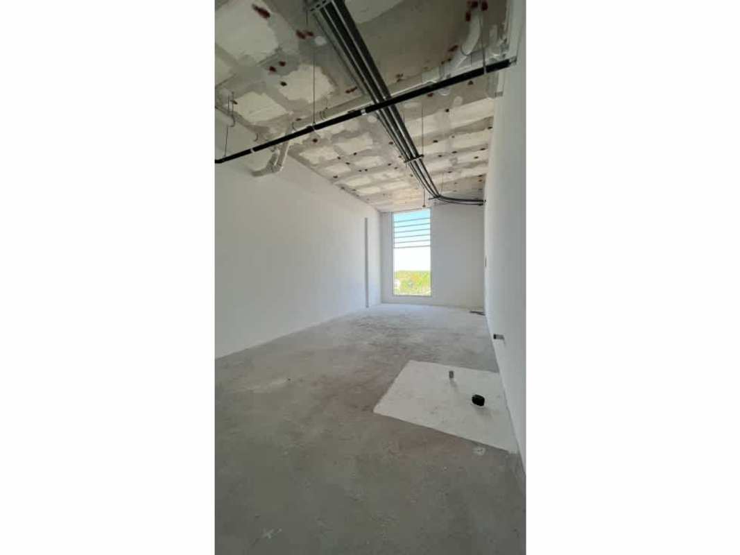 Bare concrete floor and exposed ceiling in shell unit with window to green spaces