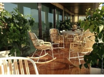Large balcony with wooden chairs, glass walls and lush plantings at Vista Mar Resort San Carlos Panama.
