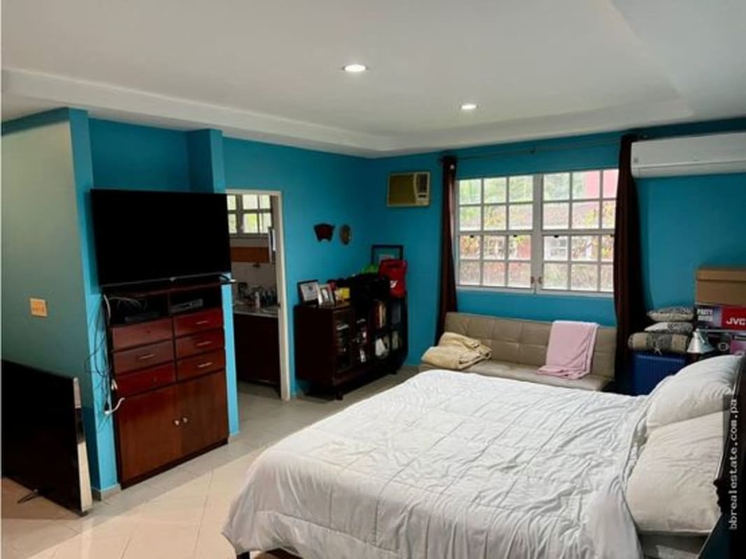 Bedroom with turquoise walls, split AC, TV, and sofa in Las Cumbres house Panama