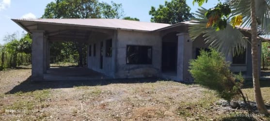 Rustic unfinished house featuring concrete walls, metal roof, carport on fenced rural property