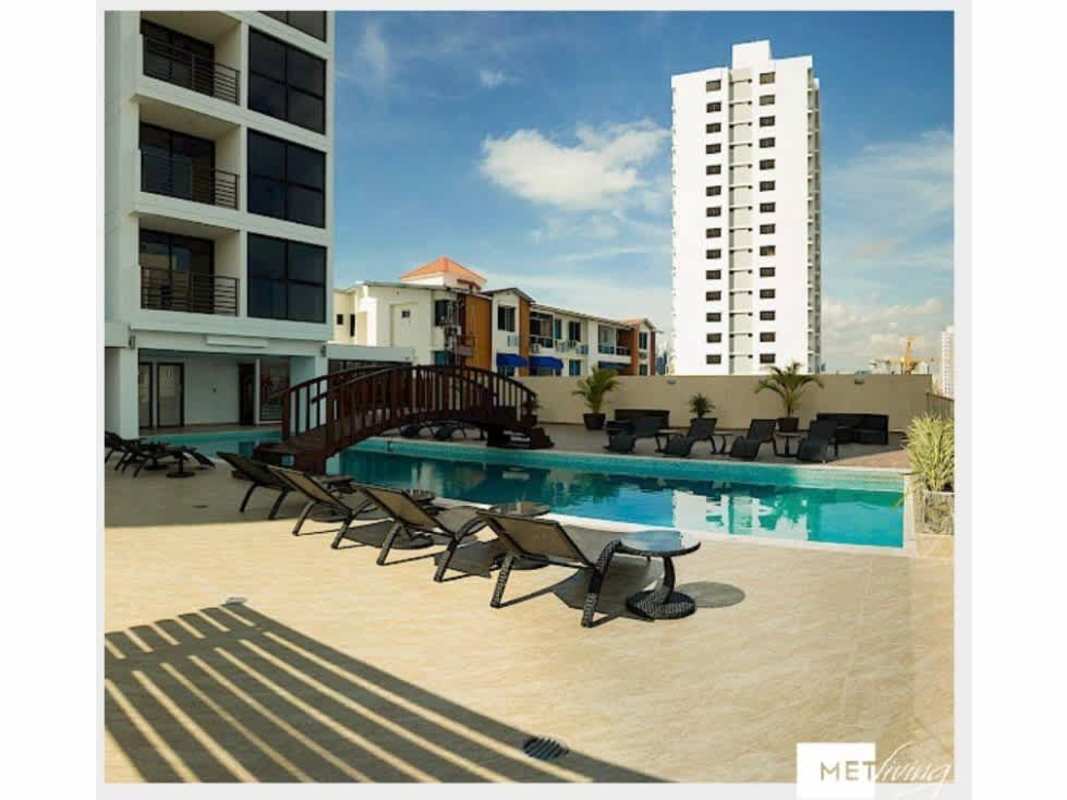 Modern apartment building with resort-style swimming pool, lounge chairs, wooden deck at PH Met Village Carrasquilla Panama