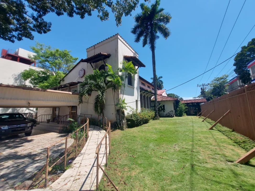 Top-down view of fenced historic lot showing gardens, parking, building with red roof in Panama City