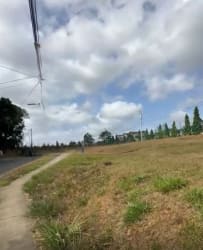 Vacant grassy lot beside sidewalk and power lines in La Chorrera commercial development area