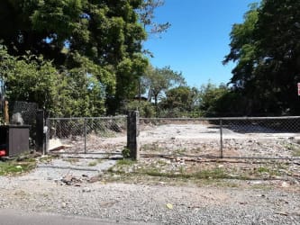 Vacant gated commercial lot surrounded by trees on busy street downtown David Chiriquí Panama