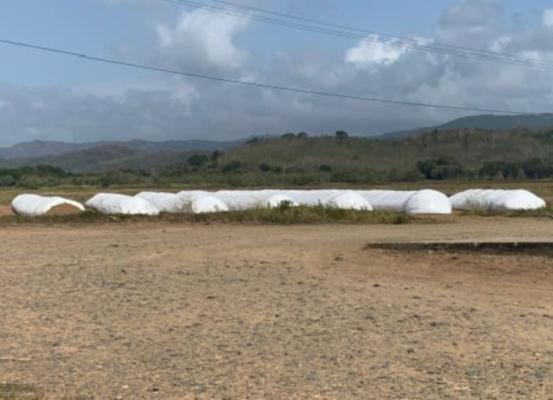 Wide farmland with hay bales covered in white plastic and mountain backdrop in Chepo Panama