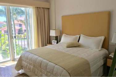 Bright coastal bedroom with balcony access overlooking garden and palm trees in Buenaventura