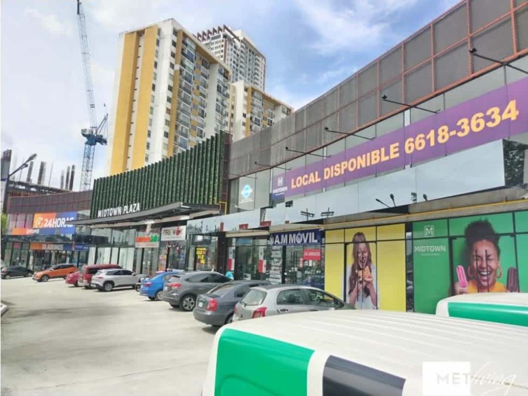 Contemporary shopping plaza at night with storefronts illuminated signage palm trees Midtown Plaza Tumba Muerto