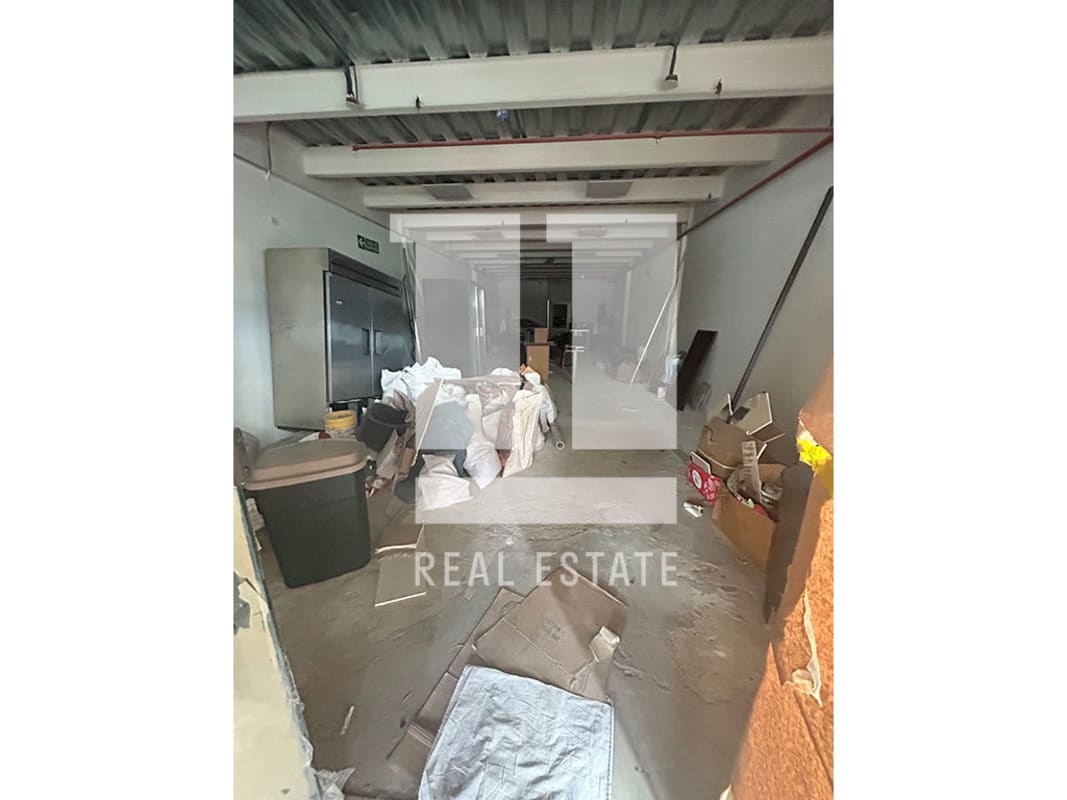 Unfinished concrete storage room with exposed ceiling beams and refrigeration in Peatonal 68