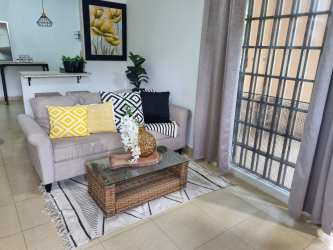 Living room with sofa, decorative pillows, glass coffee table, large window in Las Tablas house for sale