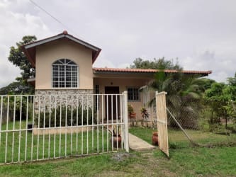 Side view of El Carate house with fenced yard, mature tree and grass lawn in Las Tablas Panama