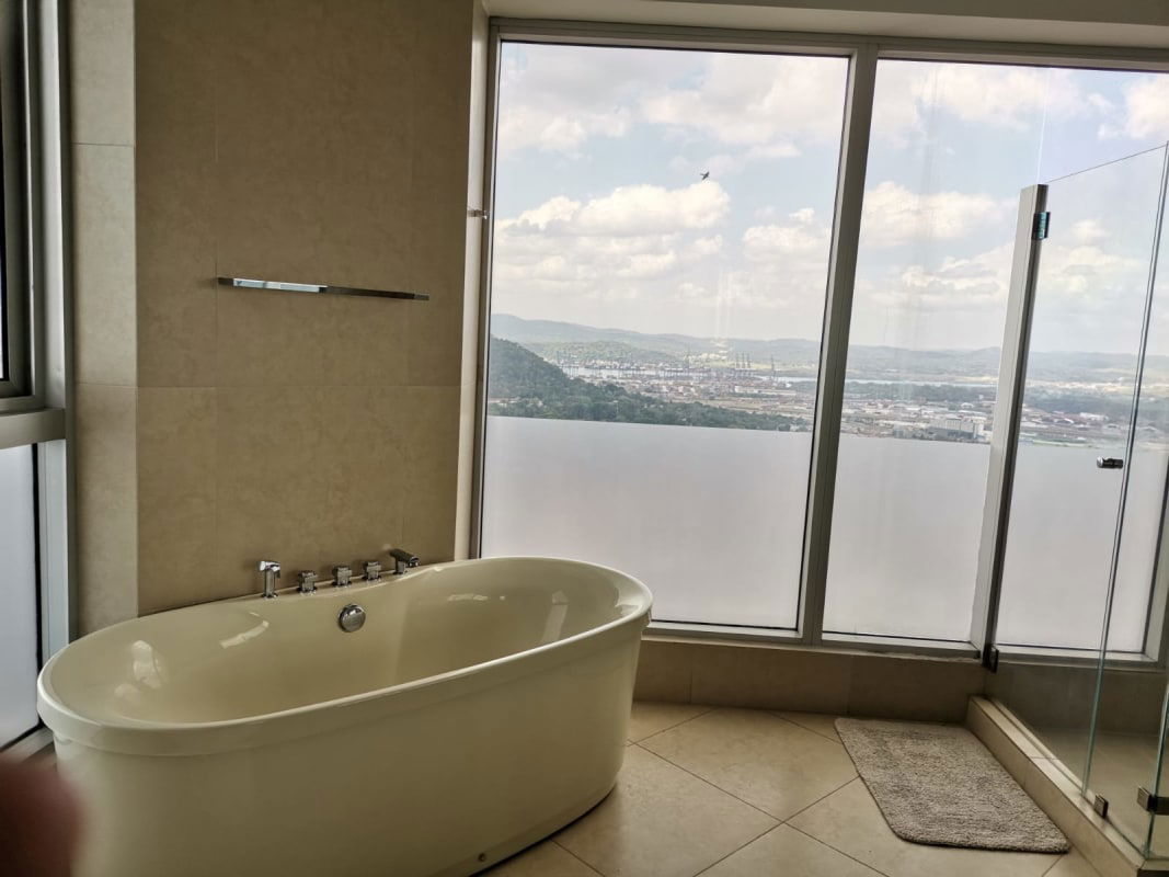 Modern bathroom with glass-enclosed shower, vanity and city panorama at PH BICSA Financial Center Panama City