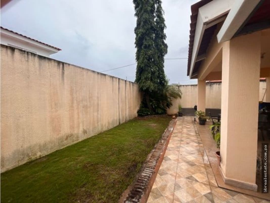 Private backyard garden with tiled walkway, green lawn, high privacy wall and covered patio PH Quintas de Versalles Panama