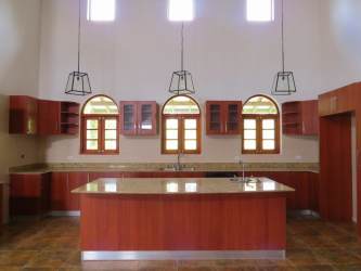 Large kitchen with wooden cabinets, stone countertops, pendant lights, and arched windows