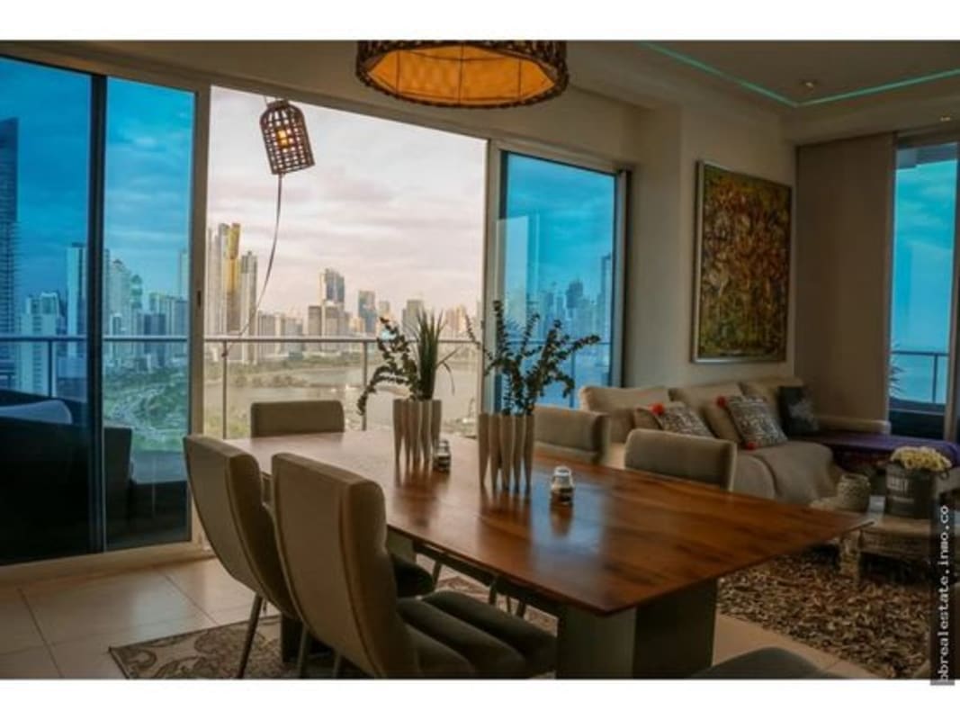 Open-plan living dining with windows and balcony facing Panama skyline and sea.