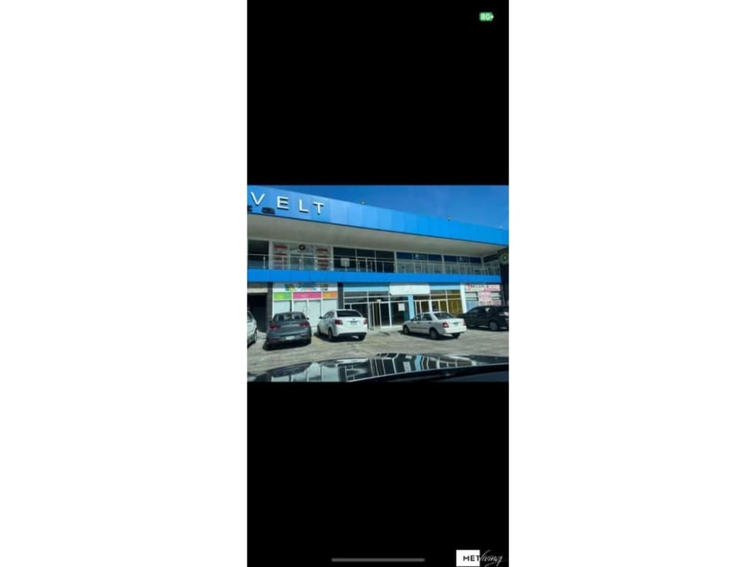Two-story commercial plaza with blue facade, glass windows, storefront signage and parking lot at San Miguelito Panama