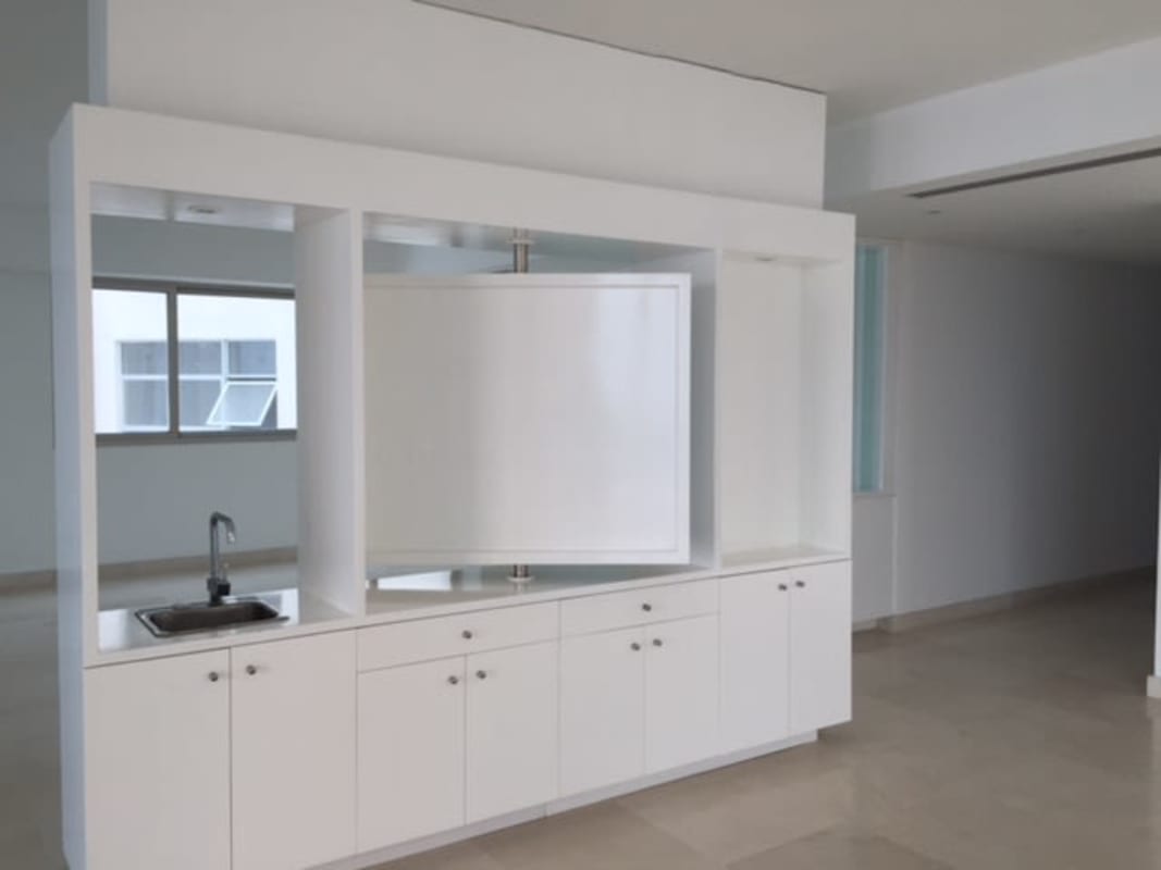 Minimalist white open-plan living with built-in cabinetry, kitchenette and rotating TV panel Punta Pacífica Panama