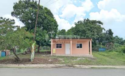 Simple peach house with covered porch, columns, tin roof and yard in San Jose Panama countryside