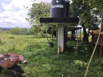 Large black water tank elevated on concrete columns on cattle farmland with mountains backdrop