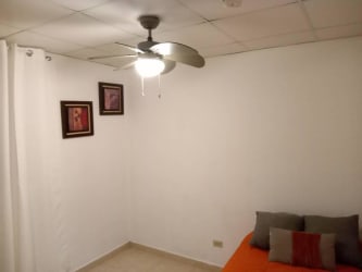 Minimalist bedroom with orange bedspread, ceiling fan, and white curtains in La Chorrera room rental