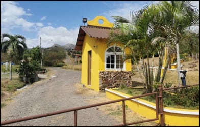 Bright yellow guard house by gated entrance with palm trees in tropical Linda Vista Paradise Sajalices Panama