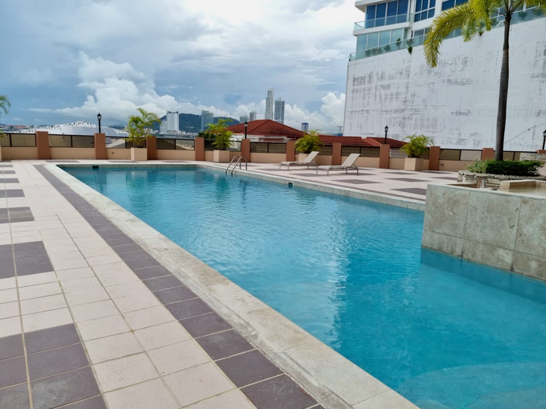 Stylish outdoor swimming pool area with sun loungers, palm trees, and skyline views at PH Maresias Panama