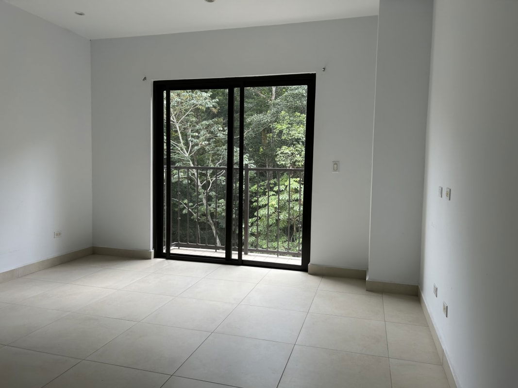Bright apartment living room with sliding glass doors to balcony overlooking greenery in PH Embassy Village Clayton Panama